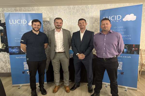 Four business professionals (L-R Ben Proudlove, Jamie Pope, Karl Wilkinson and Andrew Stanton) standing in front of Lucid Systems promotional banners at a corporate event.